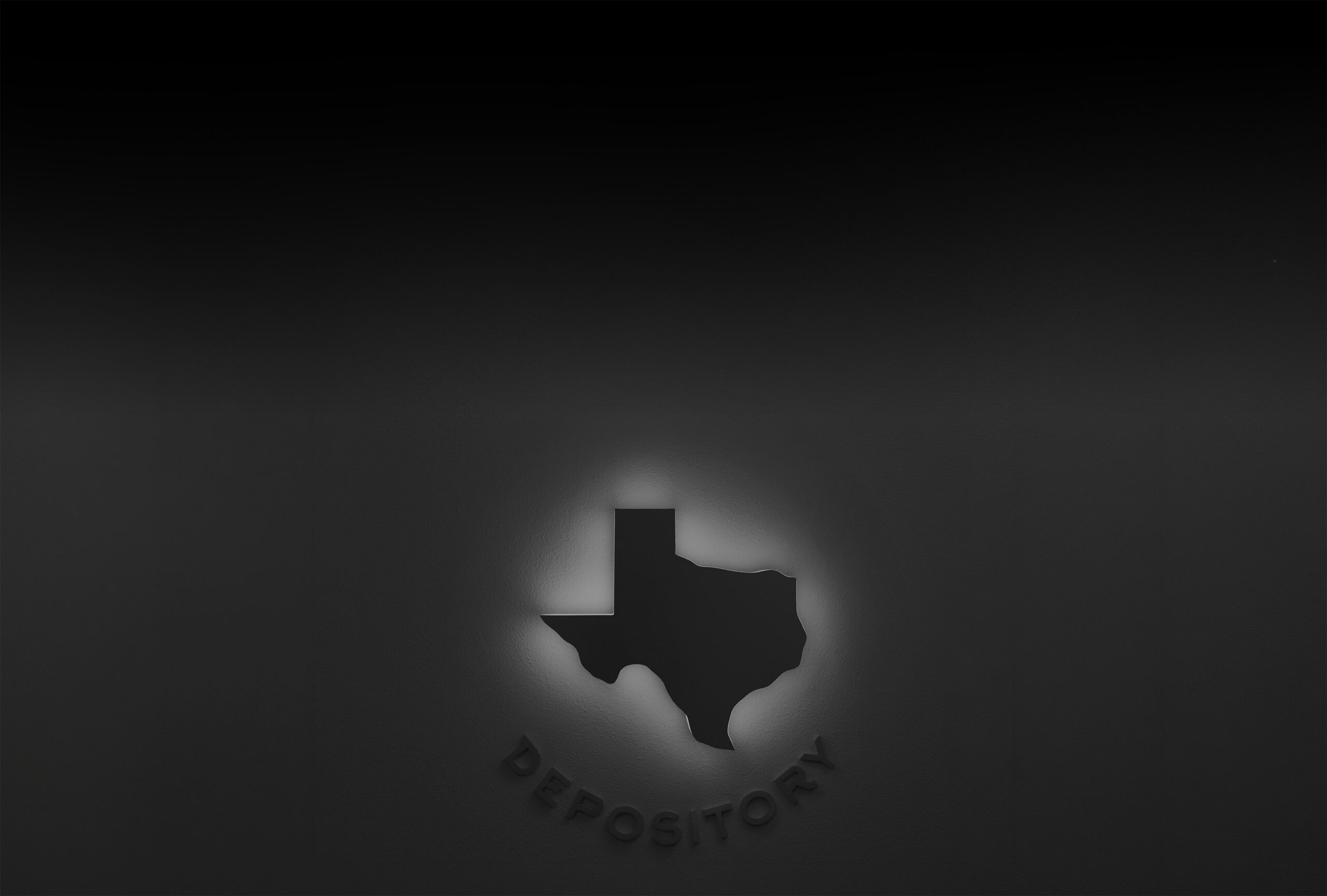 Very dark background image of a glowing Texas outline on textured wall